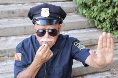 Polis kostümü giymiş yakışıklı bir adamın yakın plan portresi jesti ve açık havada ıslık çalmayı gösteriyor.