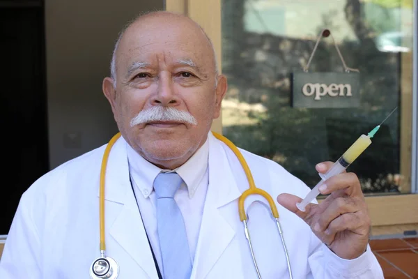 诊所玻璃门前配备听诊器和注射器的英俊老年医生特写 — 图库照片