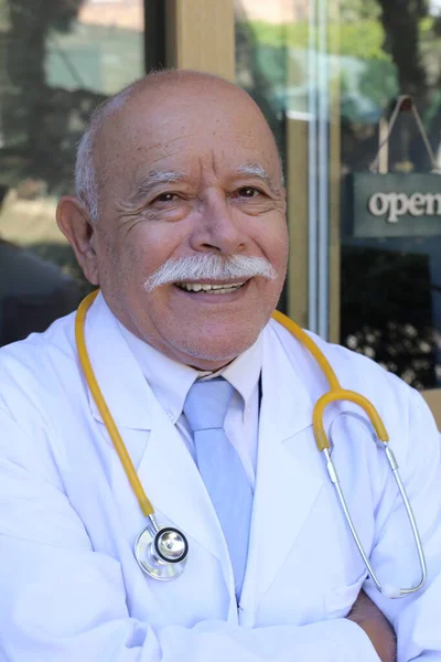 close-up portrait of handsome senior doctor with stethoscope in front of glass door of clinic