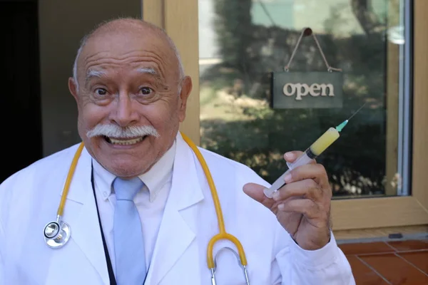 close-up portrait of handsome senior doctor with stethoscope and syringe in front of glass door of clinic