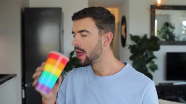 Gururlu yakışıklı adam, üzerinde gökkuşağı bayrağı olan bir bardaktan içiyor.