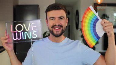 Gururlu yakışıklı adam gökkuşağı bayrağıyla elektrik işareti gösteriyor.