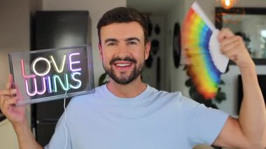 Gururlu yakışıklı adam gökkuşağı bayrağıyla elektrik işareti gösteriyor.