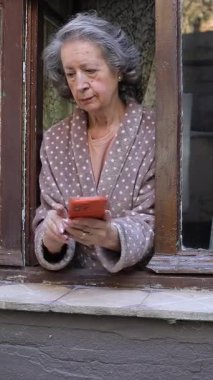 Pencereden cep telefonu kullanan yaşlı bir kadın.