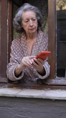 Pencereden cep telefonu kullanan yaşlı bir kadın.
