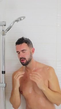 Yetişkin, beyaz bir adam, duşta suyla birlikte oturuyor.