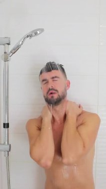 Duşun altında suyla birlikte duran genç beyaz bir adam.