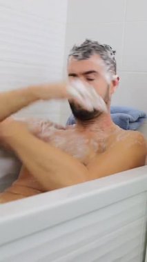 Küvette köpükle saç yıkayan mutlu bir adam. Hijyen ve erkek bakım konsepti için..