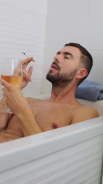 Bir adam içki ve sigara içerken küvette dinleniyor.