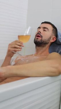 Genç adam elinde bira tutarken küvette dinleniyor..