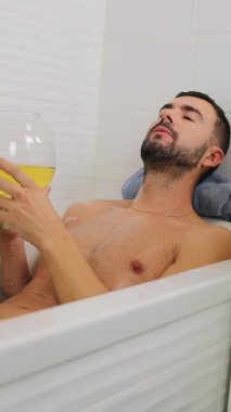 Genç adam elinde bira tutarken küvette dinleniyor..