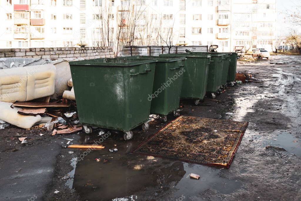 Garbage cans in a provincial Russian yard and a chic carpet in front of them lying in a puddle.