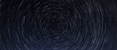 Yıldızların izleri, parlak yıldızların geceleri Kutup Yıldızı 'nın etrafında mavi gökyüzüne ve bir göktaşına karşı dönüşleri.