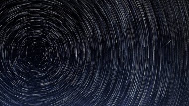 Yıldızların izleri, parlak yıldızların geceleri Kutup Yıldızı 'nın etrafında mavi gökyüzüne ve bir göktaşına karşı dönüşleri.