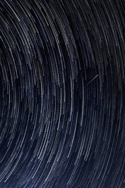 Yıldızların izleri, parlak yıldızların geceleri Kutup Yıldızı 'nın etrafında mavi gökyüzüne ve bir göktaşına karşı dönüşleri.