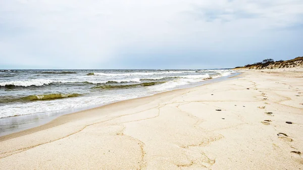 Kumsaldaki kumlarda deniz dalgaları ve ayak izleri ve bulutlu gökyüzü — Stok fotoğraf