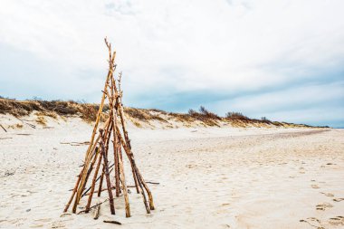 Kumlu bir sahil kıyısındaki tahta dallardan yapılmış bir sığınak iskeleti.