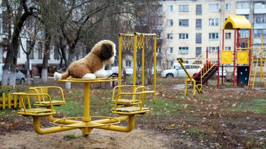 Rus bahçesinde metal salıncakta sallanan büyük yumuşak oyuncak köpek.