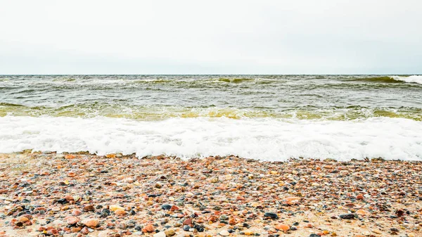 Wiele odmian skał morskich na piaszczystej plaży na tle niespokojnego Bałtyku z falami — Zdjęcie stockowe