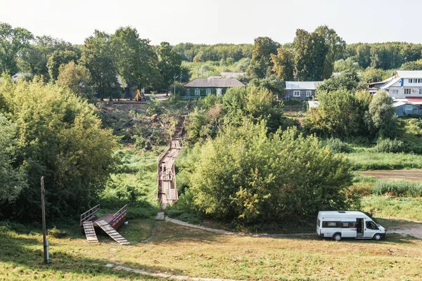 Een oude kromme brug over een riviertje op het Russische platteland in de zomer tussen groene bomen, een provinciaal landschap — Stockfoto