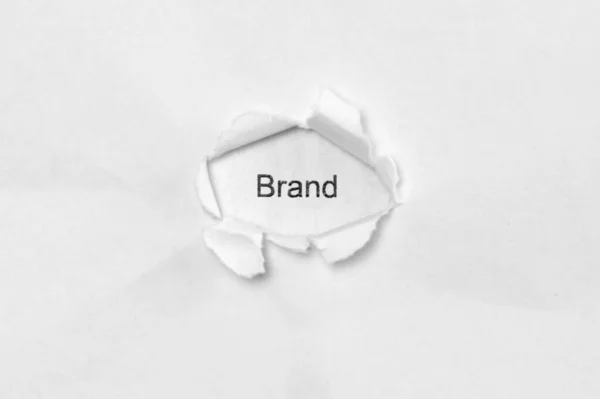 Λέξεις Brand σε λευκό απομονωμένο φόντο μέσα από την τρύπα πληγή στο χαρτί. — Φωτογραφία Αρχείου