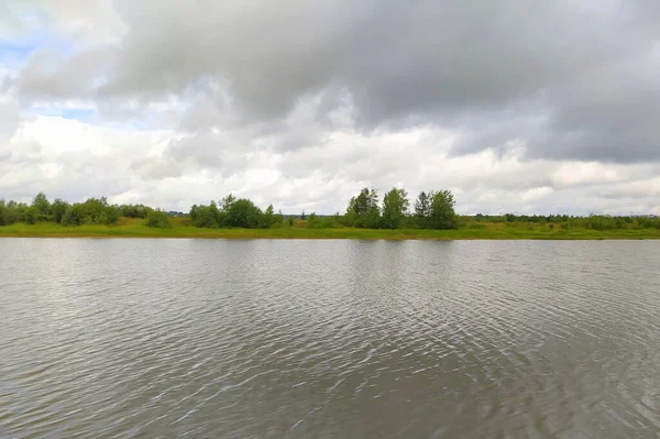 Landschaft mit Blick auf den Fluss, Sandstrand und grüne Vegetation. Wasseroberfläche mit kleinen Wellen, Ufer mit Sand und Büschen. Ein See in Russland im Sommer mit einer Küste und Bäumen. Blauer Himmel mit — Stockfoto