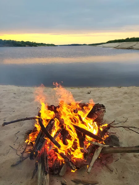 川岸でたき火をした。浜辺で火事だ。その木は砂の上で燃えている。木は水の近くで燃えている。ロシアの澄んだ青い空の下の湖の表面。自然の中でピクニック — ストック写真