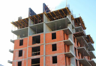 Tuğla ve betonla çok katlı bir apartman inşa ediliyor. Binanın inşaatı mavi gökyüzüne karşı. Kule vinci sarıdır.