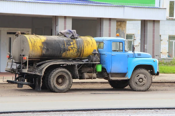 A truck with a blue cab with a yellow tank to transport molten bitumen. Road equipment on the street of the city in Russia. Repair work on the road in the spring.