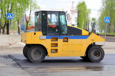Asfalt pisti sarıdır ve yeşil ağaçların arka planında lastik tekerlekler vardır. Sokakta asfalt döşeme işi.