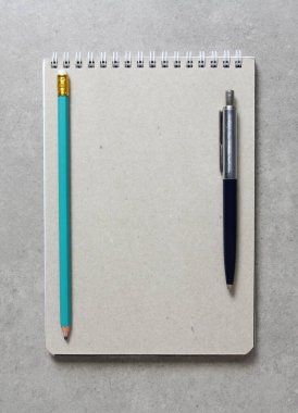Üzerinde tükenmez kalem ve açık gri beton arka planda basit yeşil bir grafit kalem bulunan bir el işi kâğıdı olan bir yay defteri. Yeni fikir, iş planı ve strateji kavramı, içeriğin geliştirilmesi ve uygulanması. Metin için boş boşluk