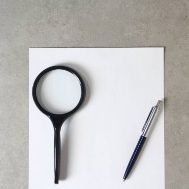 Tükenmez kalemle beyaz kağıt şablonu, büyüteç ve açık gri beton arka plan. Yeni fikir, iş planı ve strateji kavramı, içeriğin geliştirilmesi ve uygulanması. Metin için boş alanı olan stok fotoğrafı.