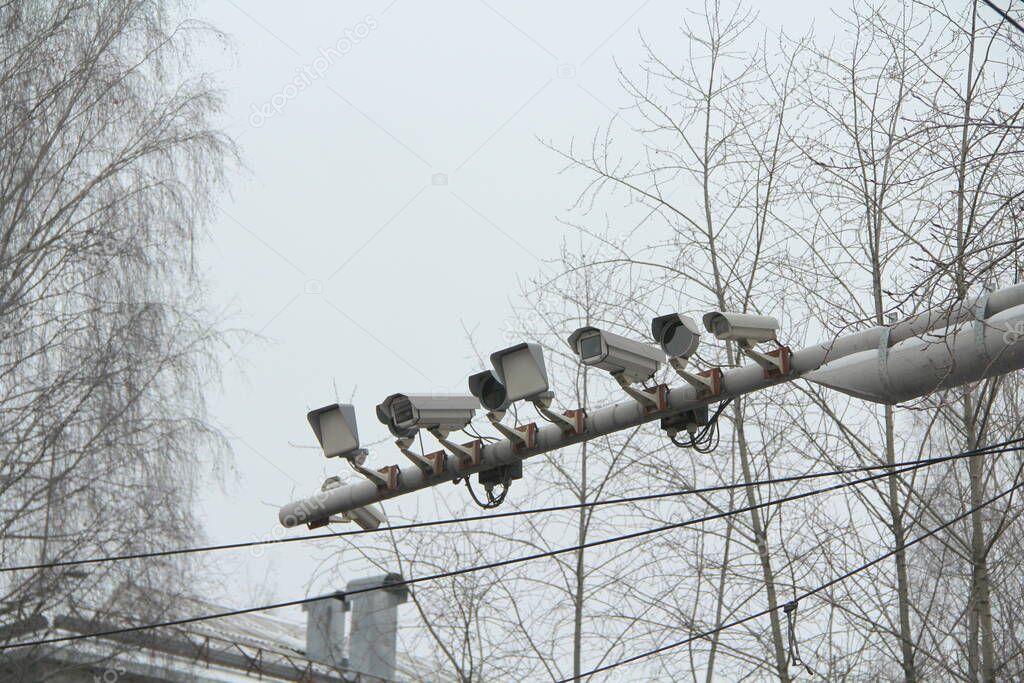 Many CCTV cameras on one crossbar above the road in the city against the bright sky
