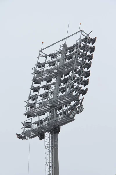 Stadium floodlight with metal pole, lighting mast, tower with floodlights in the sports stadium against the white sky