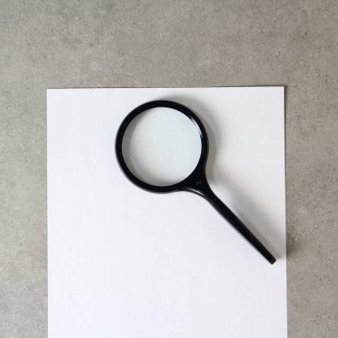 Açık gri beton zemin üzerinde büyüteç olan beyaz kağıt şablonu. Yeni fikir, iş planı ve strateji kavramı, içeriğin geliştirilmesi ve uygulanması. Metin için boş alanı olan stok fotoğrafı.