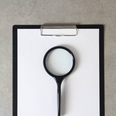 Beyaz kağıt şablonu açık gri beton arka planda büyüteç ile siyah bir tablet ve bir şarjör. Yeni fikir, iş planı ve strateji kavramı, içeriğin geliştirilmesi ve uygulanması. Metin için boş alanı olan stok fotoğrafı.