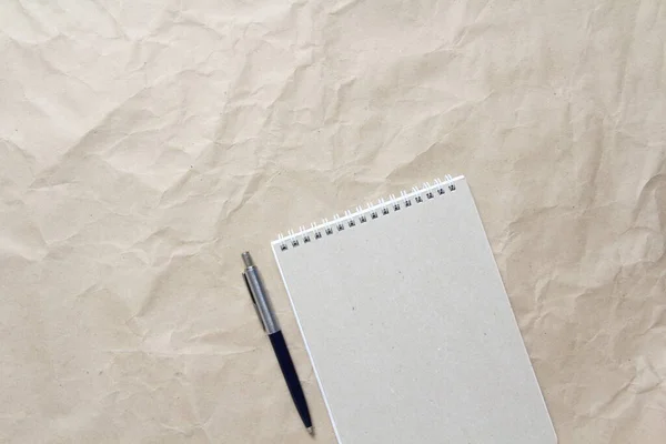 Bloco de notas cinza com mola e caneta enroladas brancas em um fundo de papel artesanal bege amassado — Fotografia de Stock