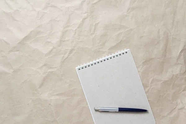 Grijze notitieblok met witte opgerolde veer en pen op een achtergrond van beige verfrommeld ambachtelijk papier — Stockfoto