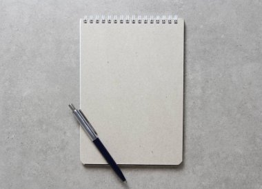 Açık gri beton arkaplanlı tükenmez kalemle kaplı bir el işi kâğıdı olan bir yay defteri. Yeni fikir, iş planı ve strateji kavramı, içeriğin geliştirilmesi ve uygulanması. Metin için boş boşluk.