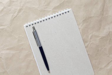 Beyaz sarmalanmış yay ve bej buruşuk el işi kağıdının arka planında kalem olan gri not defteri. Metin ve tasarım için boş boşluk