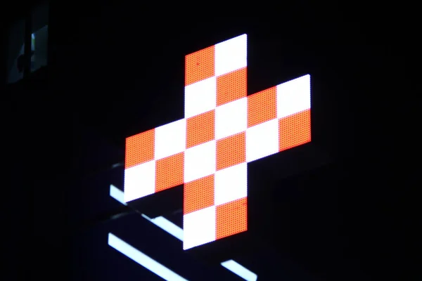 Glowing pixel cross of LED lamps on black background. Cross with a pattern in white and orange symbol of health, medicine, self-care. Stock photo with empty space for text and design.