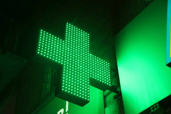 Glowing pixel cross of LED lamps on black background. Green cross symbol of health, medicine, self-care. Stock photo with empty space for text and design.
