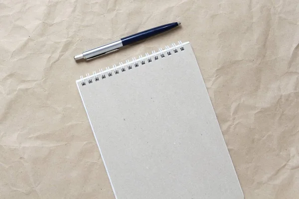 白いコイル状の春とベージュのしわクラフト紙の背景にペンで灰色のメモ帳 テキストとデザインのための空のスペースと — ストック写真