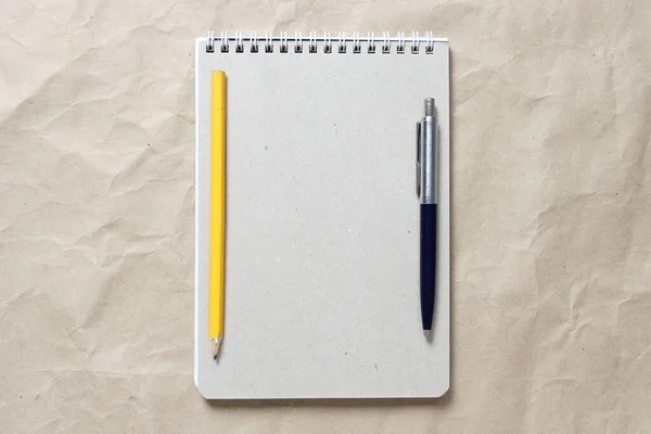 灰色的笔记本 白色卷曲的弹簧和笔和铅笔在米色皱折的工艺纸的背景 有空白的文字和设计空间 — 图库照片