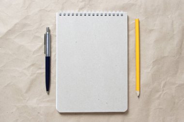 Beyaz sarmal yay, kalem ve kalemle bej buruşuk el işi kağıdının arka planında gri bir not defteri. Metin ve tasarım için boş boşluk