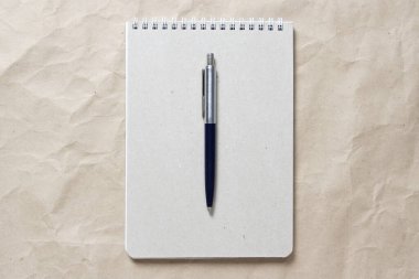 Beyaz sarmalanmış yay ve bej buruşuk el işi kağıdının arka planında kalem olan gri not defteri. Metin ve tasarım için boş boşluk