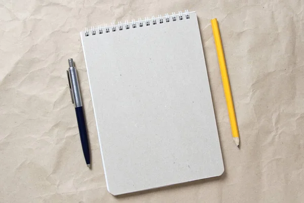 ベージュのクランプクラフト紙の背景に白いコイル状の春とペンと鉛筆で灰色のメモ帳 テキストとデザインのための空のスペースと — ストック写真