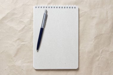 Beyaz sarmalanmış yay ve bej buruşuk el işi kağıdının arka planında kalem olan gri not defteri. Metin ve tasarım için boş boşluk