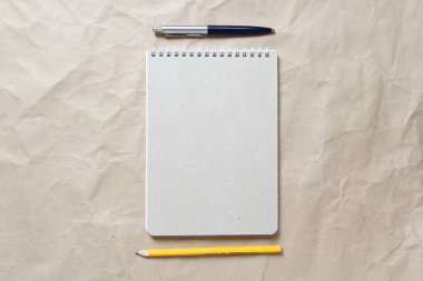 Beyaz sarmal yay, kalem ve kalemle bej buruşuk el işi kağıdının arka planında gri bir not defteri. Metin ve tasarım için boş boşluk