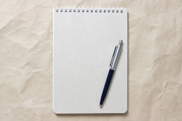 Gray notepad with white coiled spring and pen on a background of beige crumpled craft paper